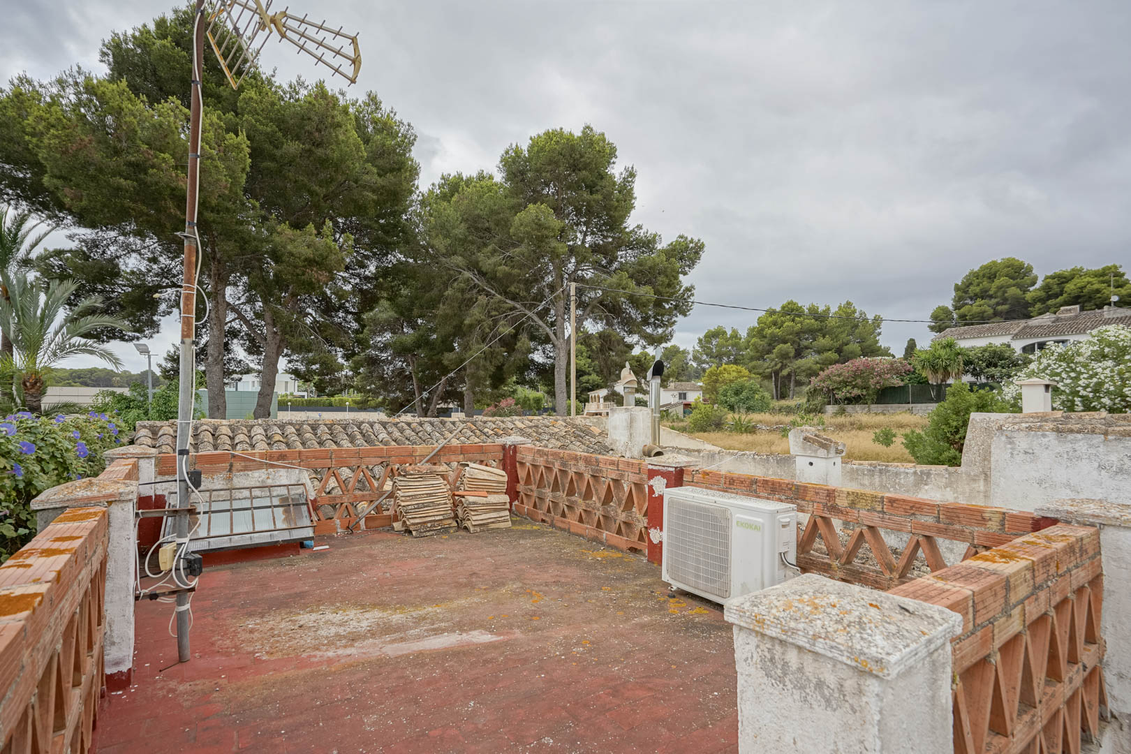 Dakterras met rode tegelvloer en decoratieve bakstenen balustrades. De ruimte biedt uitzicht op volwassen pijnbomen en de omliggende woonwijk.