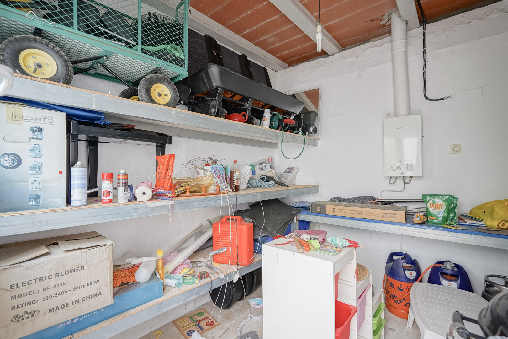 Functionele bergruimte voorzien van opbergschappen, een gasgeiser aan de wand en een traditioneel plafond met houten balken en terracotta tegels.