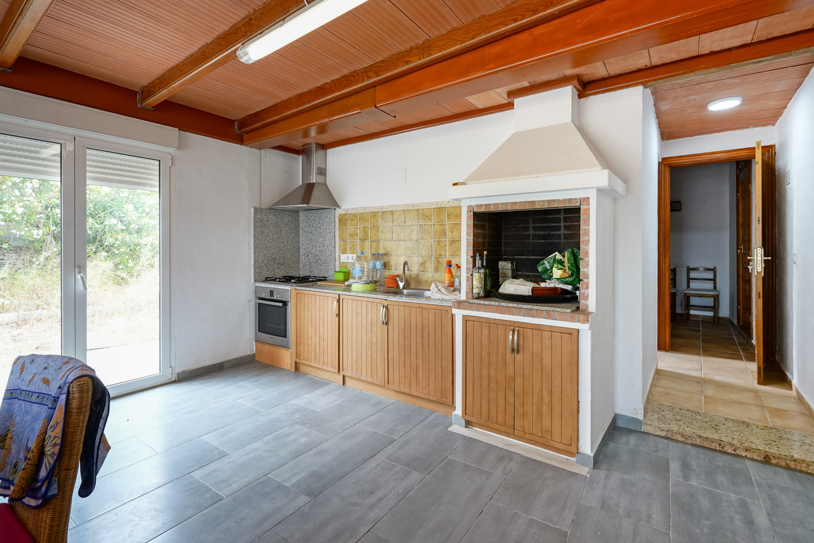 Functionele keuken met houten plafond en balken, voorzien van een ingebouwde barbecue, granieten werkbladen en directe toegang tot de tuin.