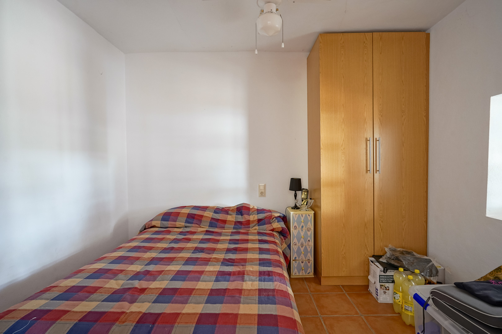 Functionele slaapkamer met terracotta tegelvloer, een hoge houten kledingkast en witte muren die het natuurlijke licht optimaliseren.
