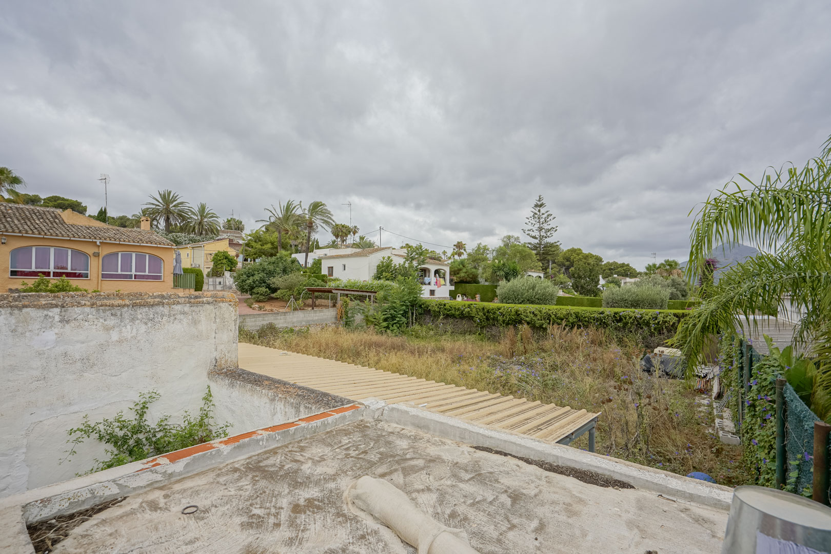 Verhoogd perspectief op het perceel van 2.600 m² met natuurlijke begroeiing, omringd door naburige villa's en de contouren van de Montgó.
