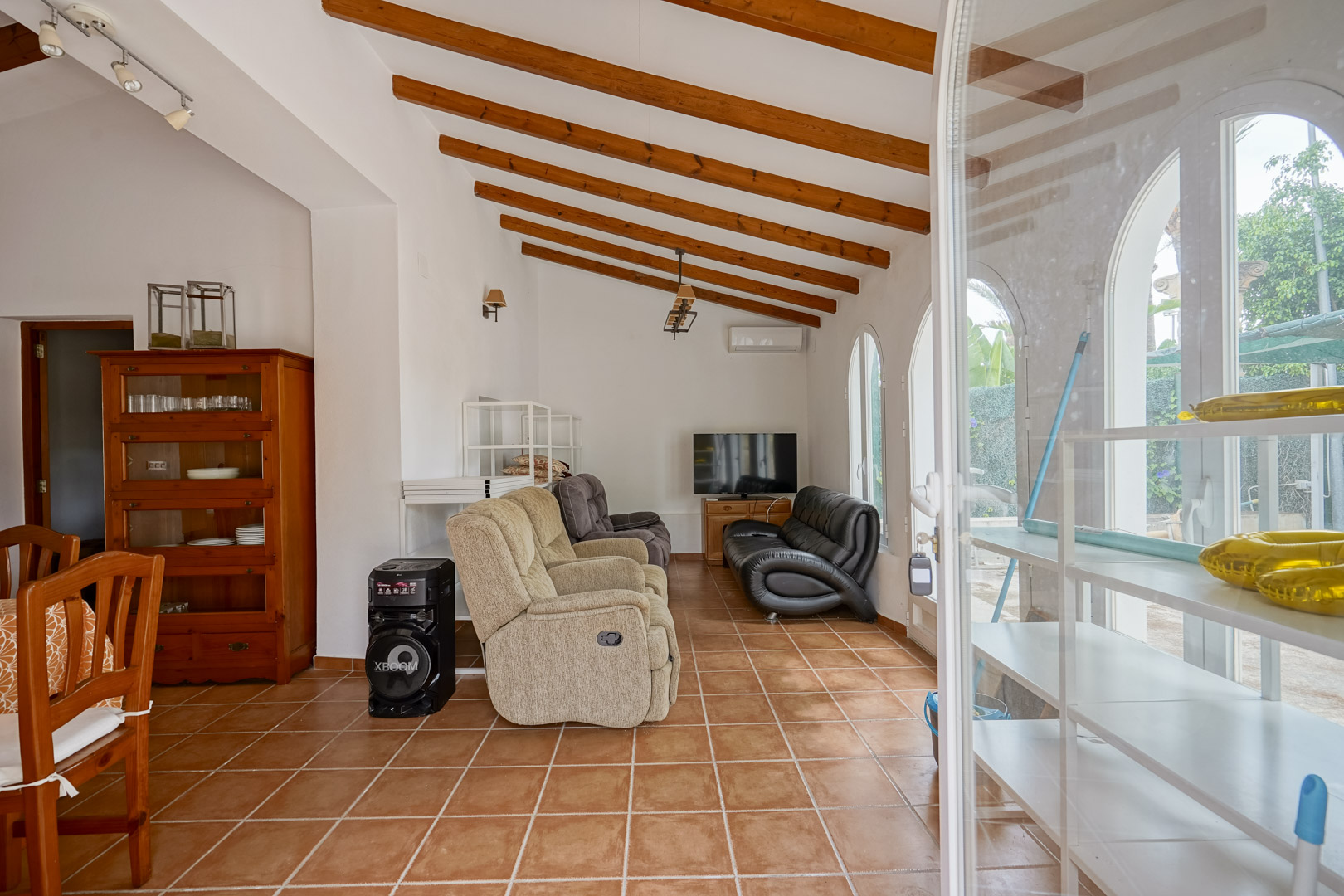 Woonkamer met een schuin plafond met houten balken, terracotta vloertegels en karakteristieke boogramen met veel lichtinval.