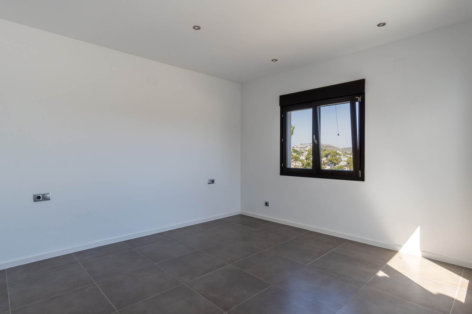 Minimalistische slaapkamer met grijze porseleinen tegelvloer, inbouw-ledverlichting en een donker aluminium raam met uitzicht op de omgeving.