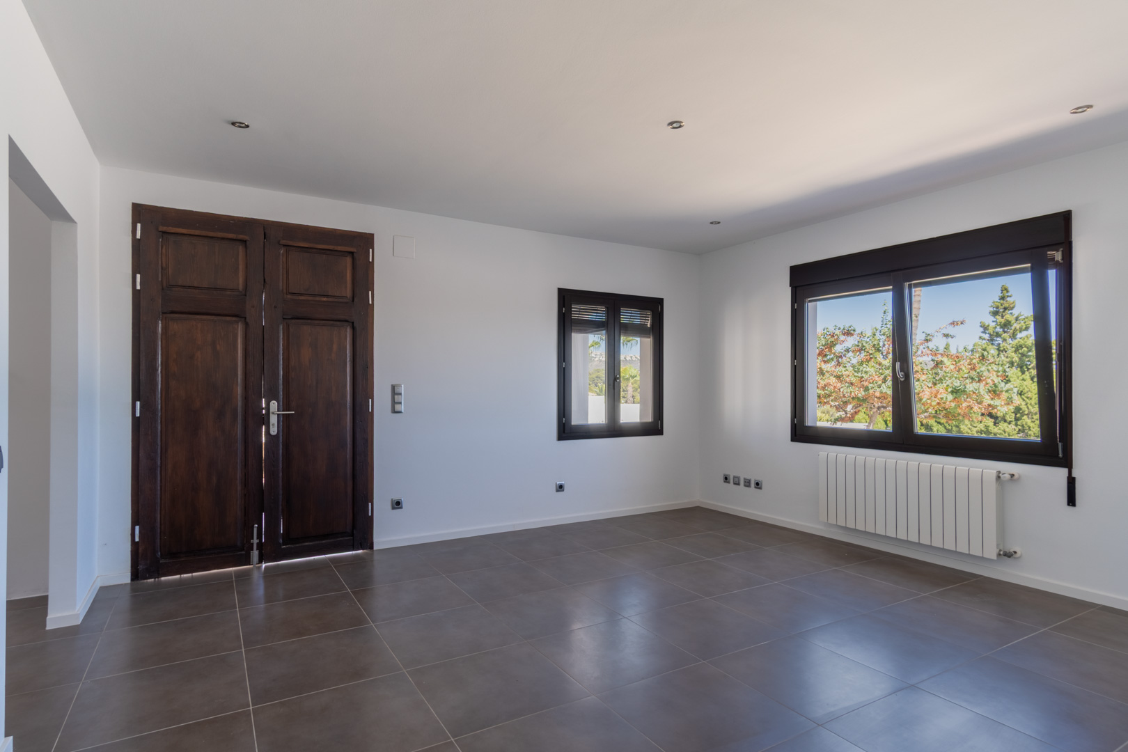 Woonruimte met gerestaureerde antieke houten deur, aluminium ramen met houtlook, radiatorverwarming en grootformaat grijze keramische vloertegels.