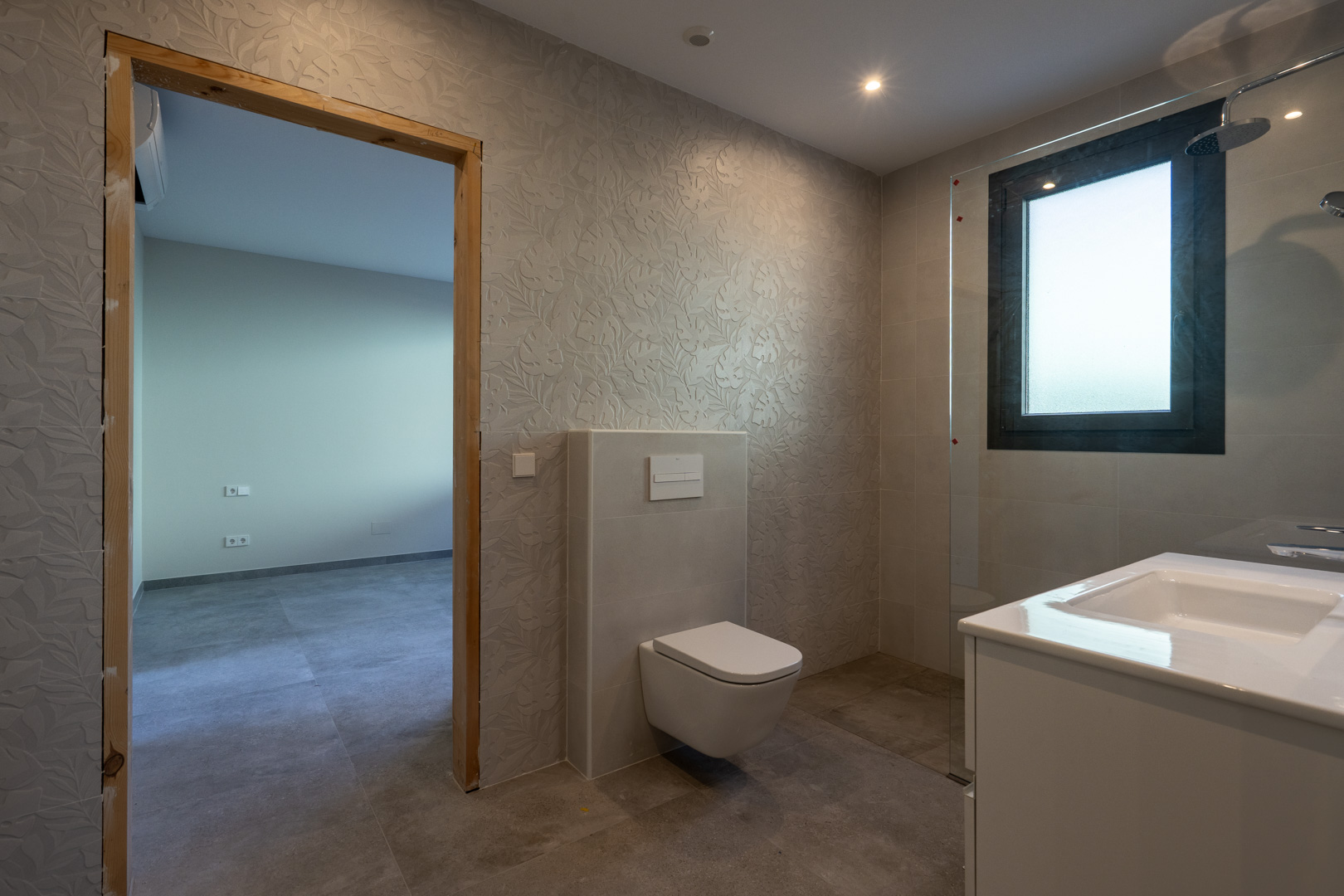 Detail van een moderne badkamer met getextureerde muren en glazen douche.