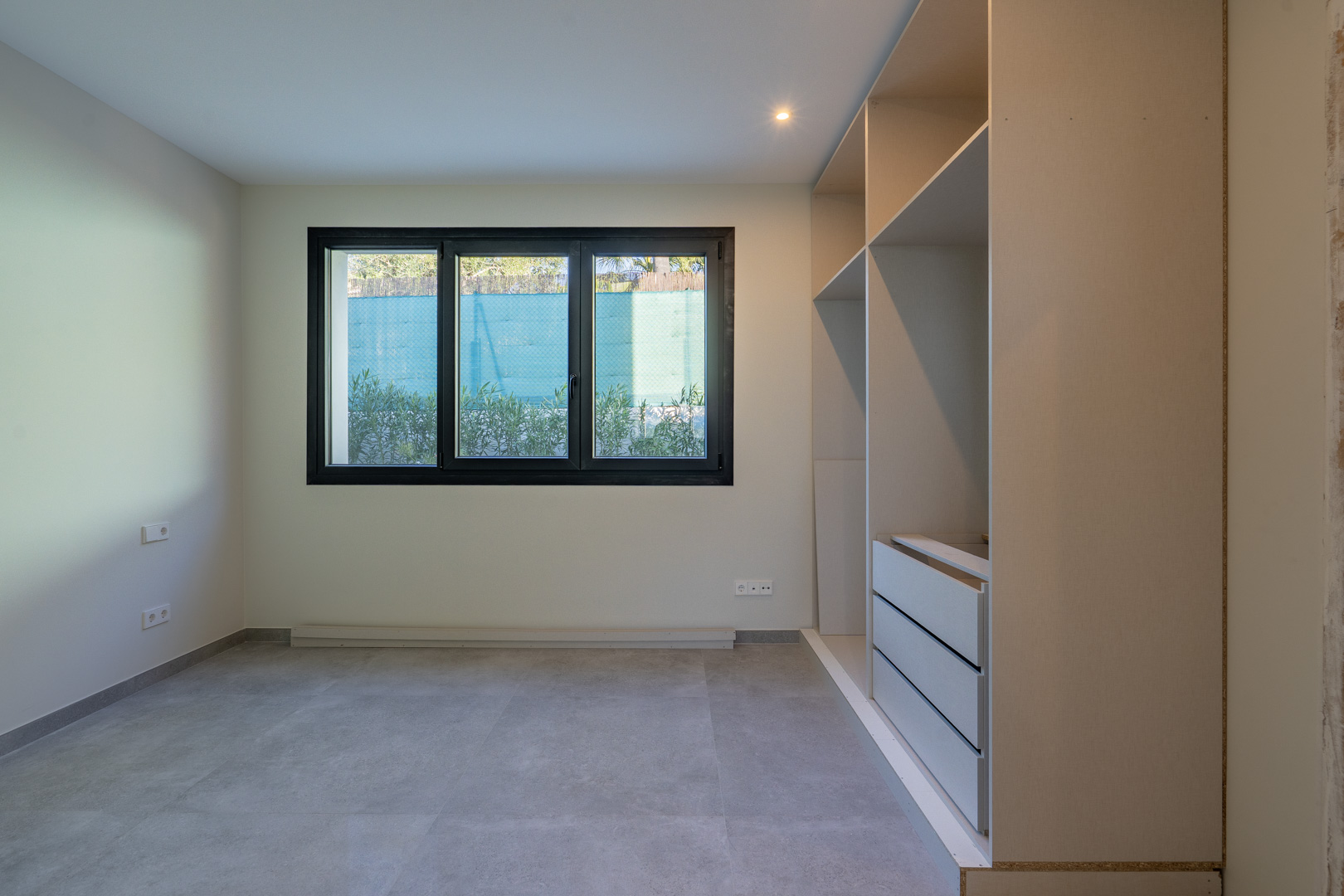 Lichte slaapkamer met driedubbel glas en een inbouwkast zonder deuren. Grijze tegelvloer.