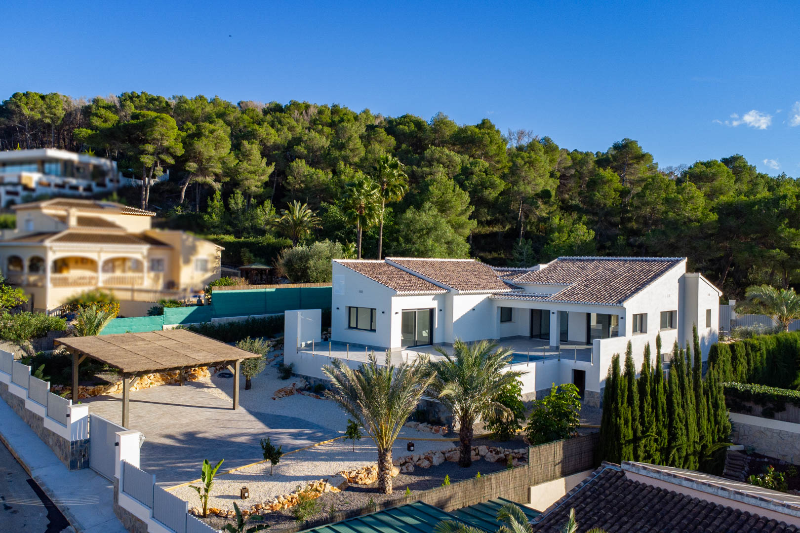 Luchtfoto van moderne villa met bruine dakpannen, witte gevel en overdekte carport in Jávea, omgeven door groen.