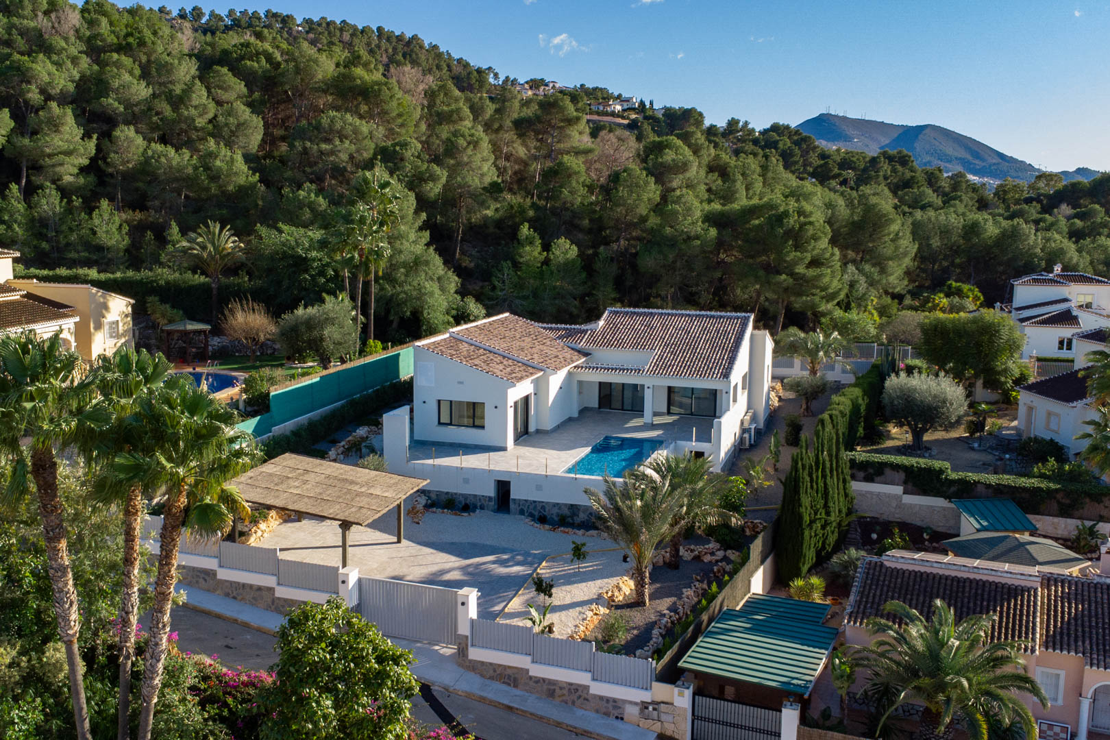 Luchtfoto van moderne villa met zwembad, omgeven door weelderig groen en een overdekte parkeerplaats in Jávea.