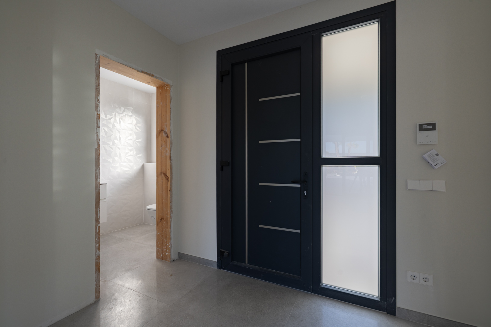 Moderne entree met design deur en toegang tot een toilet met gestructureerde tegelwand.