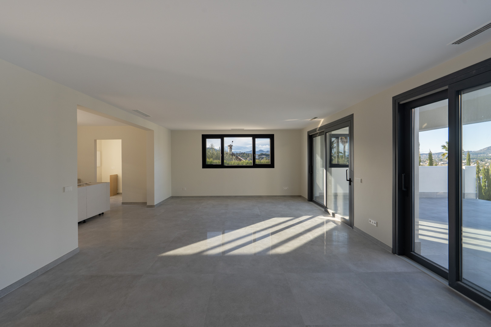 Ruime woonkamer met tegelvloer, panoramisch raam en toegang tot het terras in Jávea.
