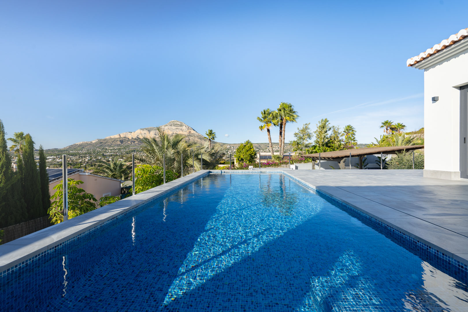 Uitzicht op het privézwembad met blauwe tegels, grijs betegeld terras en uitzicht op de bergen in Jávea.