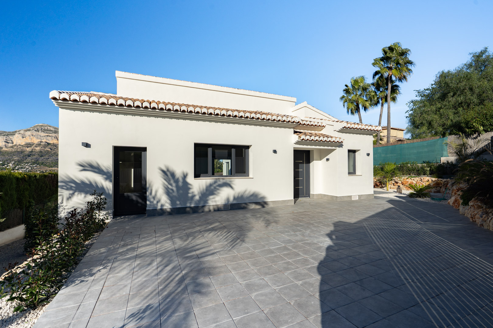 Villa-exterieur met een witte gevel, terracotta dakpannen en een grijze tegelvloer. Berg uitzicht.