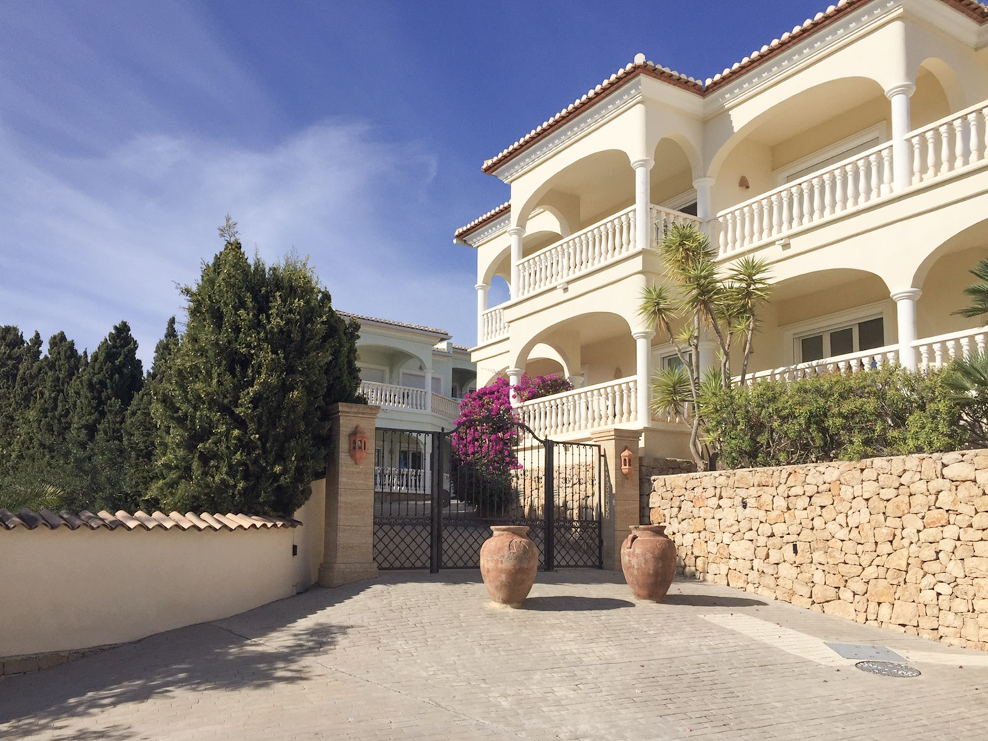Hoofdingang met smeedijzeren poort, natuurstenen muren en mediterrane architectuur met boogvormige terrassen en decoratieve terracotta amforen.