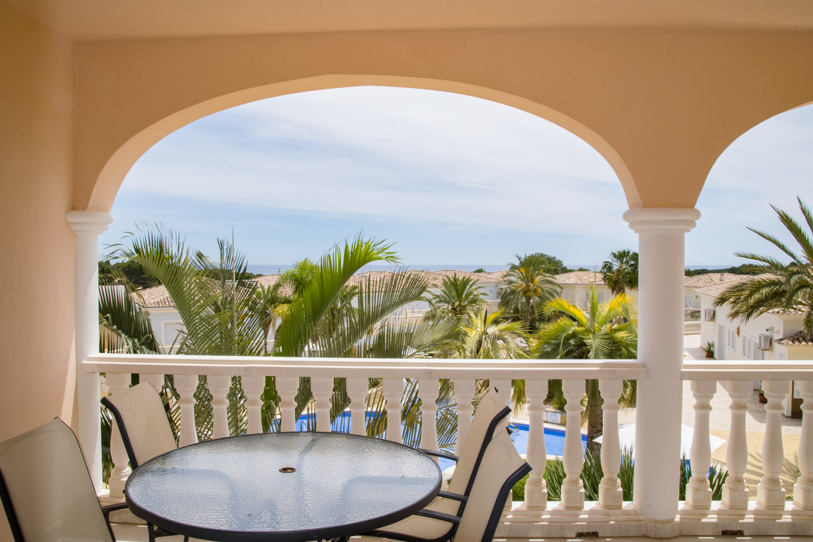 Overdekt terras met klassieke bogen en balustrades, voorzien van een eethoek. Uitzicht op de mediterrane tuinen, het lagune-zwembad en de verre zee.