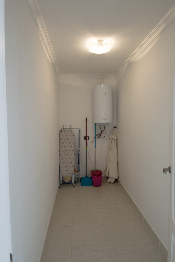 Praktische bergruimte met elektrische boiler, opbergruimte voor schoonmaakspullen en een tegelvloer met sierlijsten aan het plafond.