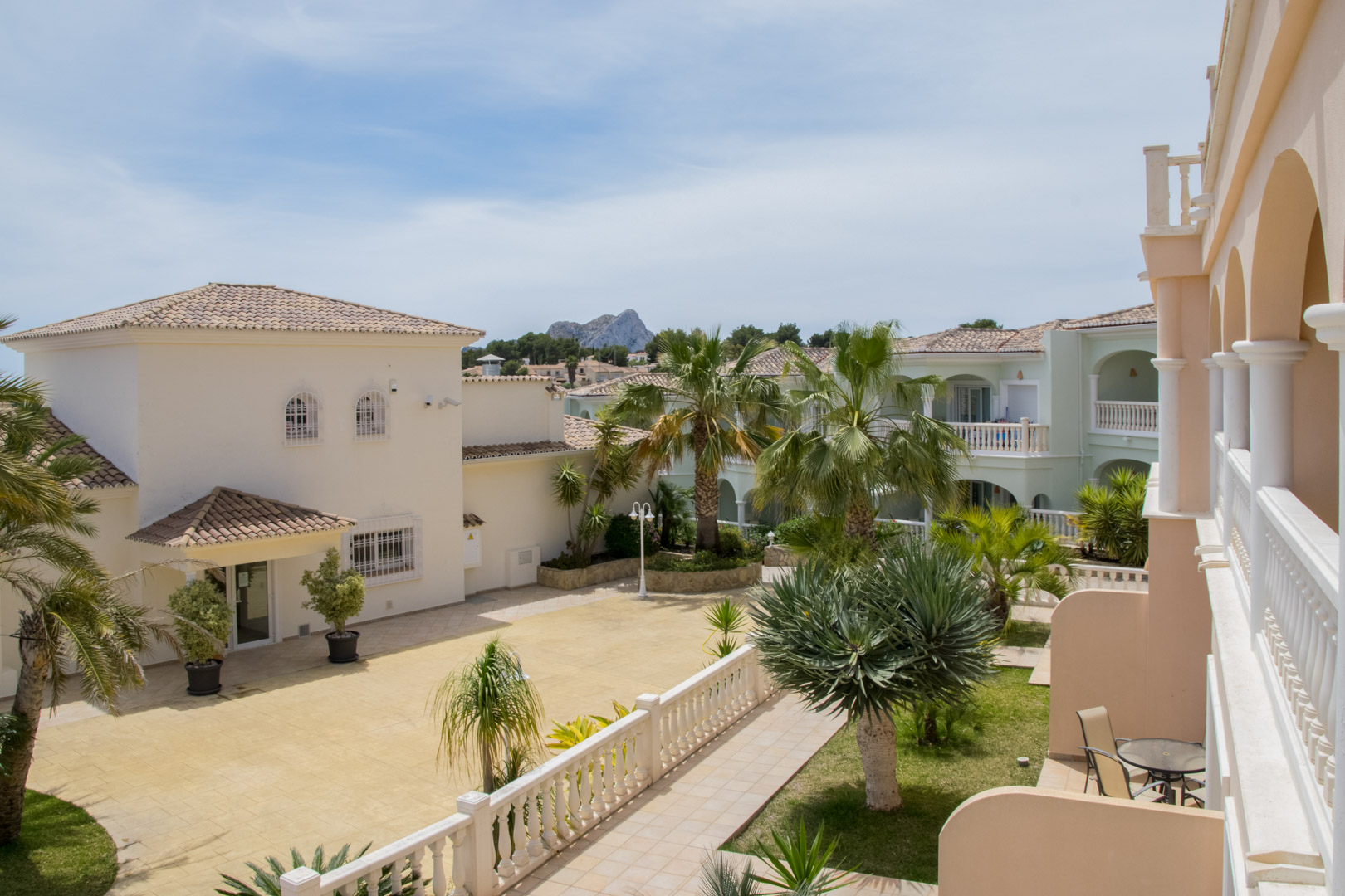 Uitzicht vanaf het terras op de mediterrane architectuur, aangelegde tuinen met palmbomen en een ver uitzicht op de Peñón de Ifach.