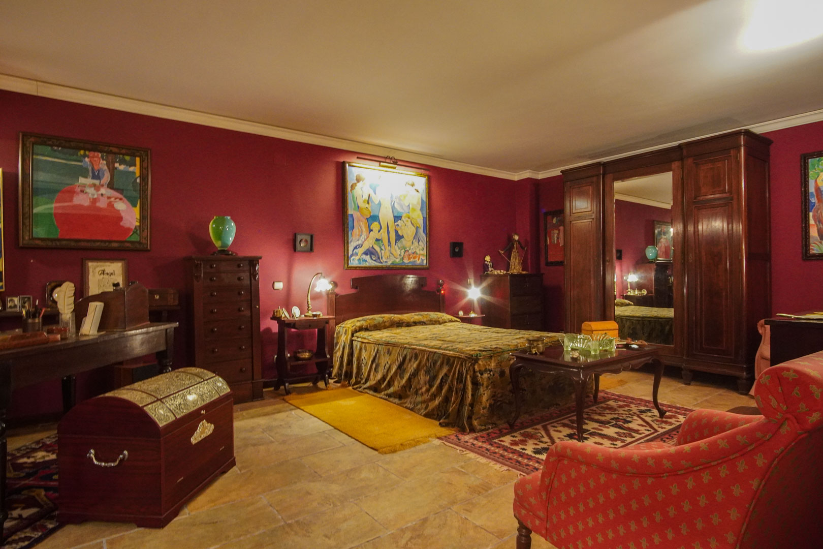 Klassieke slaapkamer met bordeauxrode muren, donkerhouten antiek meubilair, natuurstenen vloer en een grote kledingkast met centrale spiegel.