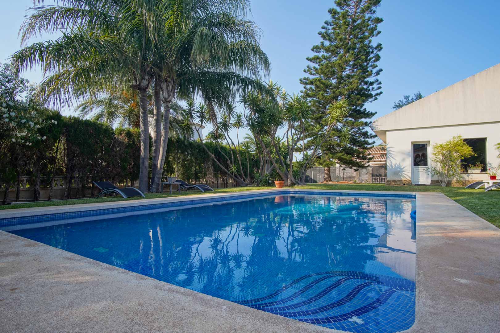 Privézwembad met blauwe mozaïektegels en ingebouwde trap, gelegen in een mediterrane tuin met palmbomen, gazon en hagen die zorgen voor volledige privacy.
