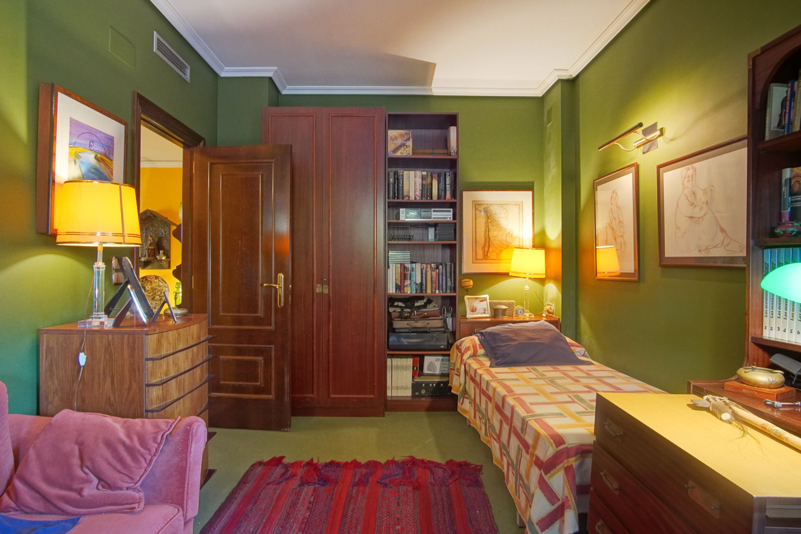 Slaapkamer met groene muren, klassiek donkerhouten meubilair en eenpersoonsbed. Voorzien van ingebouwde boekenkast, sfeerverlichting en centrale airconditioning.