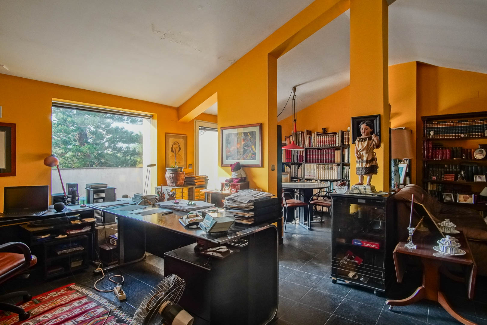 Werkkamer op de zolderverdieping met schuine plafonds, mosterdgele muren, een ruim bureau en ingebouwde boekenkasten met veel natuurlijk licht.