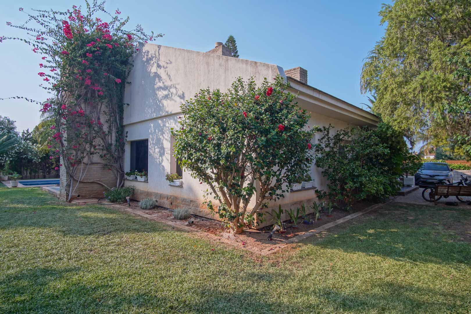 Zijgevel van de villa met een natuurlijk gazon, klimmende bougainville op een stenen muur en mediterrane struiken in de tuin.