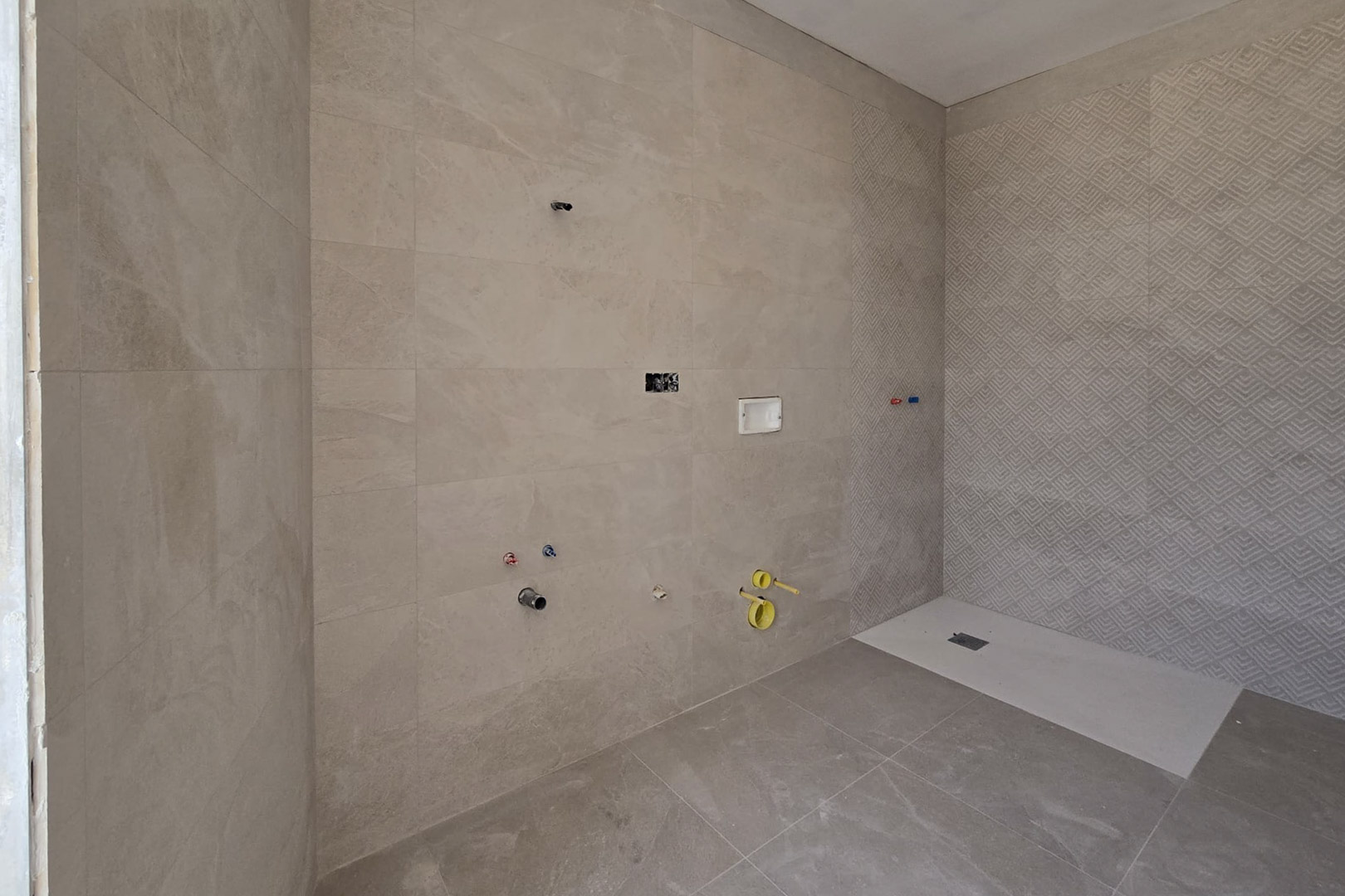 Badkamer in aanbouw met zandkleurige porseleinen tegels, een geometrische accentmuur in de douche en een extra platte witte douchebak.