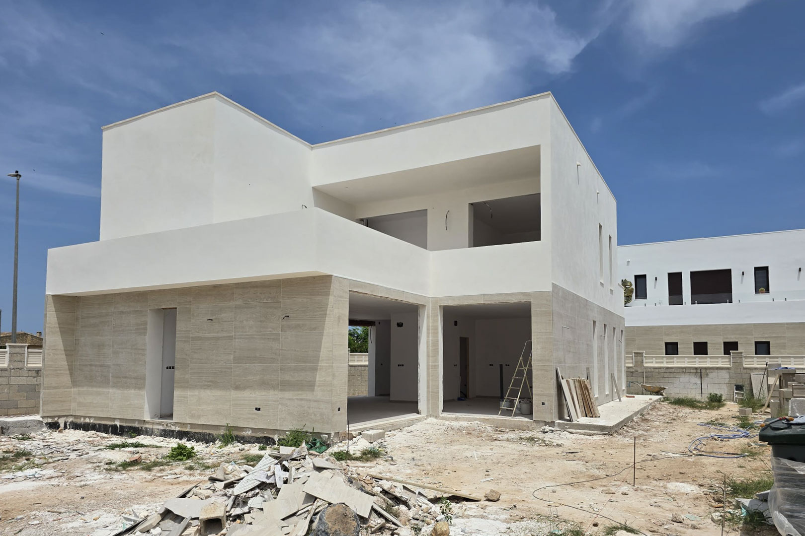 Buitenaanzicht van een moderne villa in aanbouw met natuurstenen gevelbekleding op de begane grond, witte geometrische volumes en grote openingen voor raampartijen.