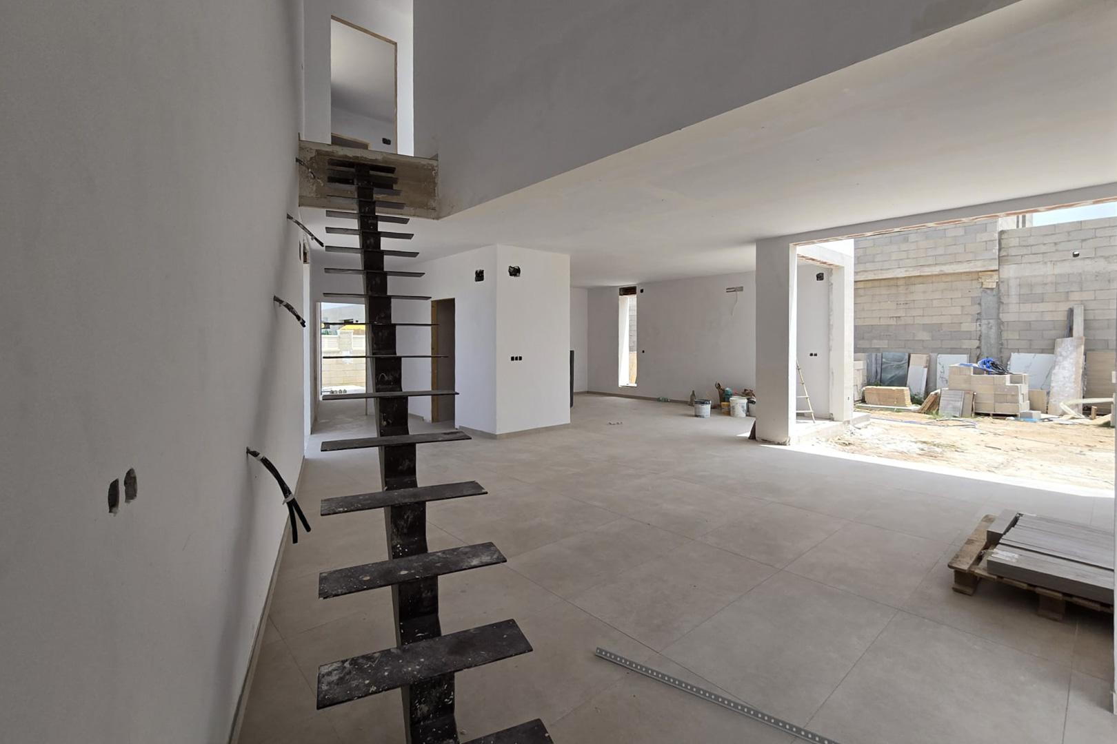Open interieur in aanbouw met een industriële metalen trap, grootformaat vloertegels en een vide die zorgt voor een ruimtelijk effect en veel licht.