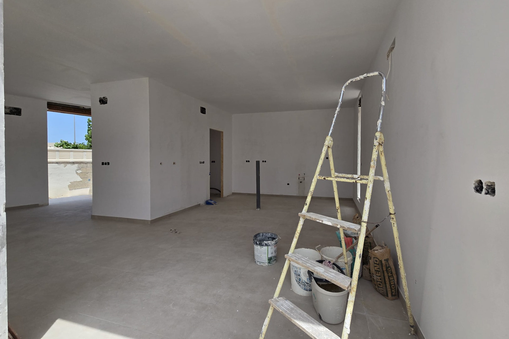 Open interieur in de afwerkingsfase met grootformaat keramische vloertegels en witte muren. De elektrische pre-installaties en toegang tot buiten zijn zichtbaar.