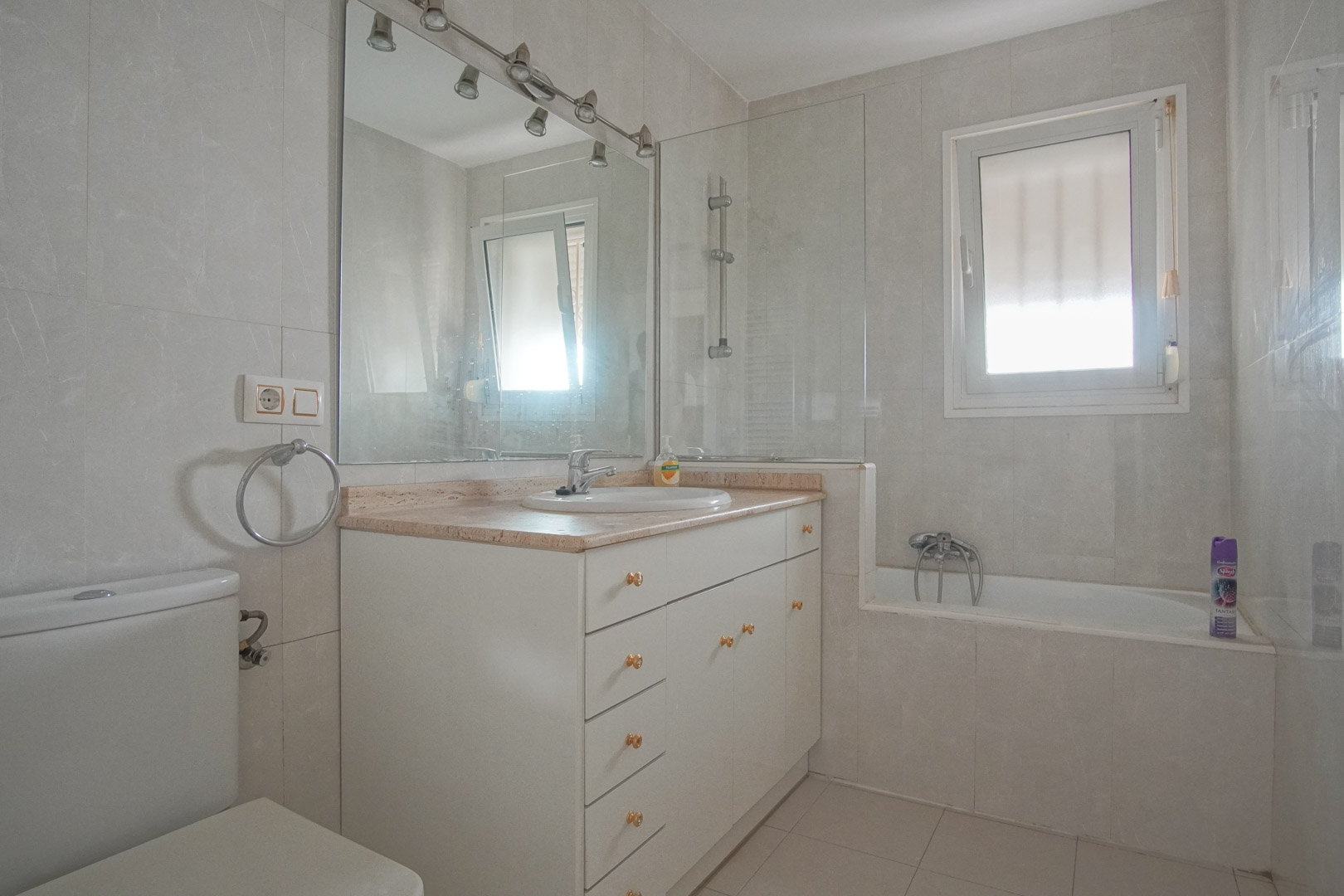 Badkamer met wit wastafelmeubel, marmeren blad en ligbad met glazen douchescherm. Voorzien van natuurlijke lichtinval en ventilatie via een raam.