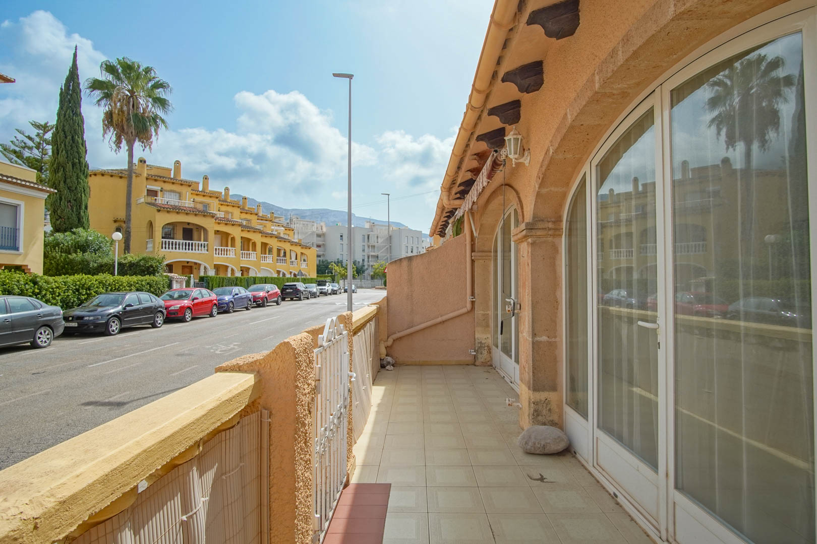 Buitenterras met keramische tegels en grote boogvormige glazen deuren, met uitzicht op de rustige woonstraat en de omliggende bebouwing in Dénia.