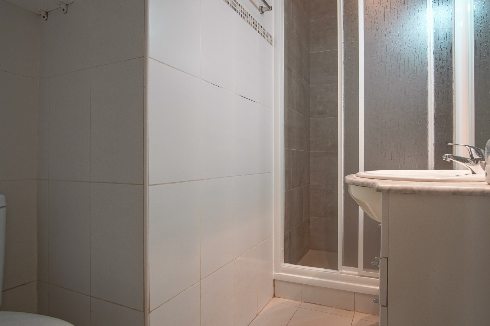 Functionele badkamer met wit betegelde wanden, een douchecabine met matglas en een wastafel op een marmeren blad.