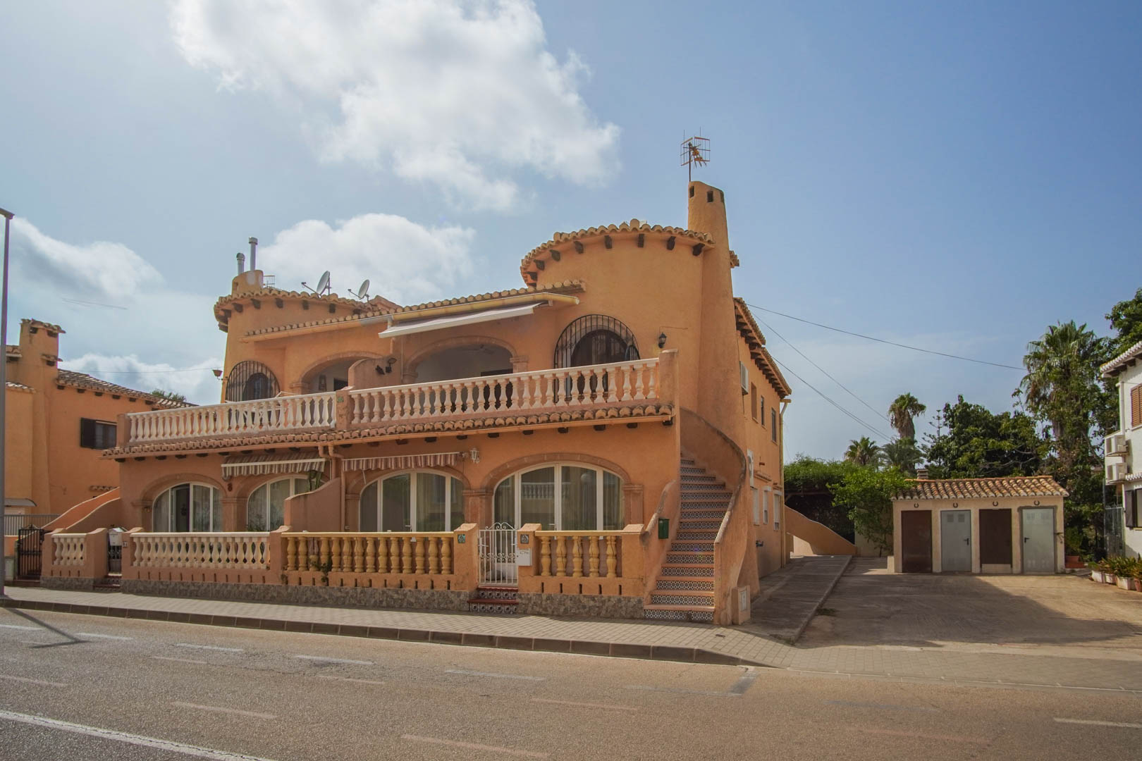 Mediterrane gevel met boogvensters, stenen balustrades en een buitentrap met decoratieve tegels, gelegen op straatniveau.
