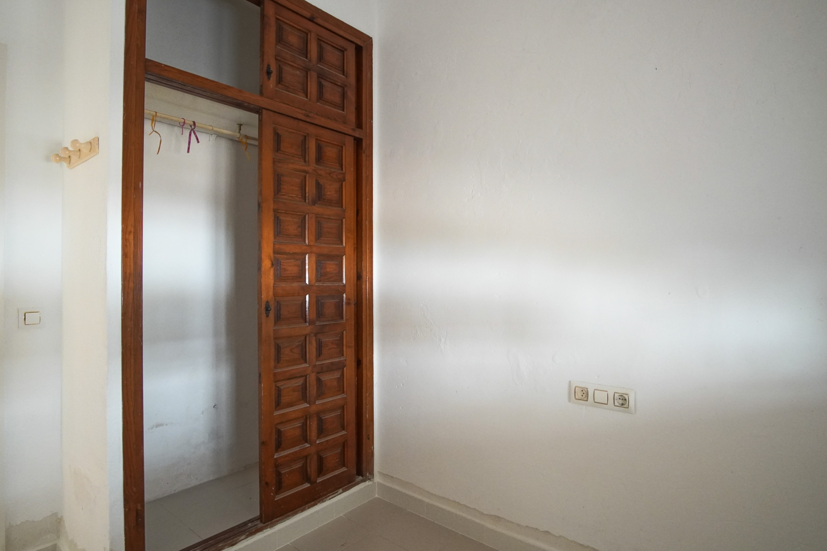 Slaapkamer met een ingebouwde donkerhouten kledingkast met paneelschuifdeuren. De ruimte is voorzien van witte muren met textuur en een tegelvloer.