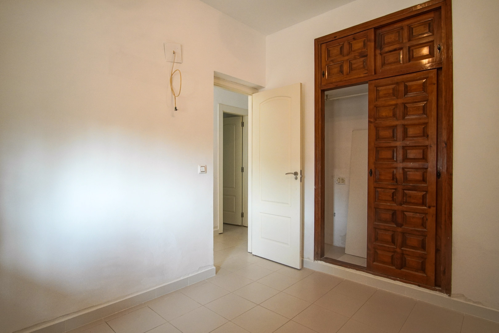 Slaapkamer met een ingebouwde kast van bewerkt hout en een tegelvloer. De ruimte staat in verbinding met de gang en biedt mogelijkheden voor renovatie.