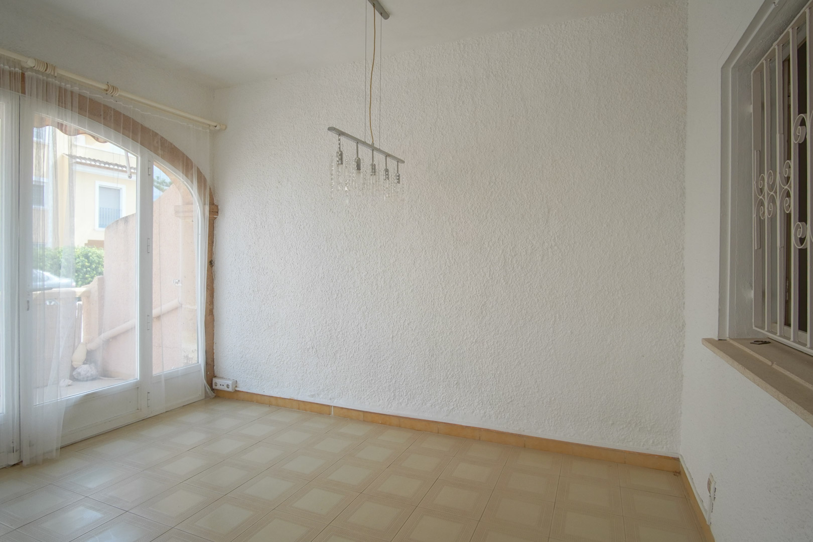 Woonkamer met gestructureerde witte muren, tegelvloer en een karakteristieke boogdeur die zorgt voor veel lichtinval.