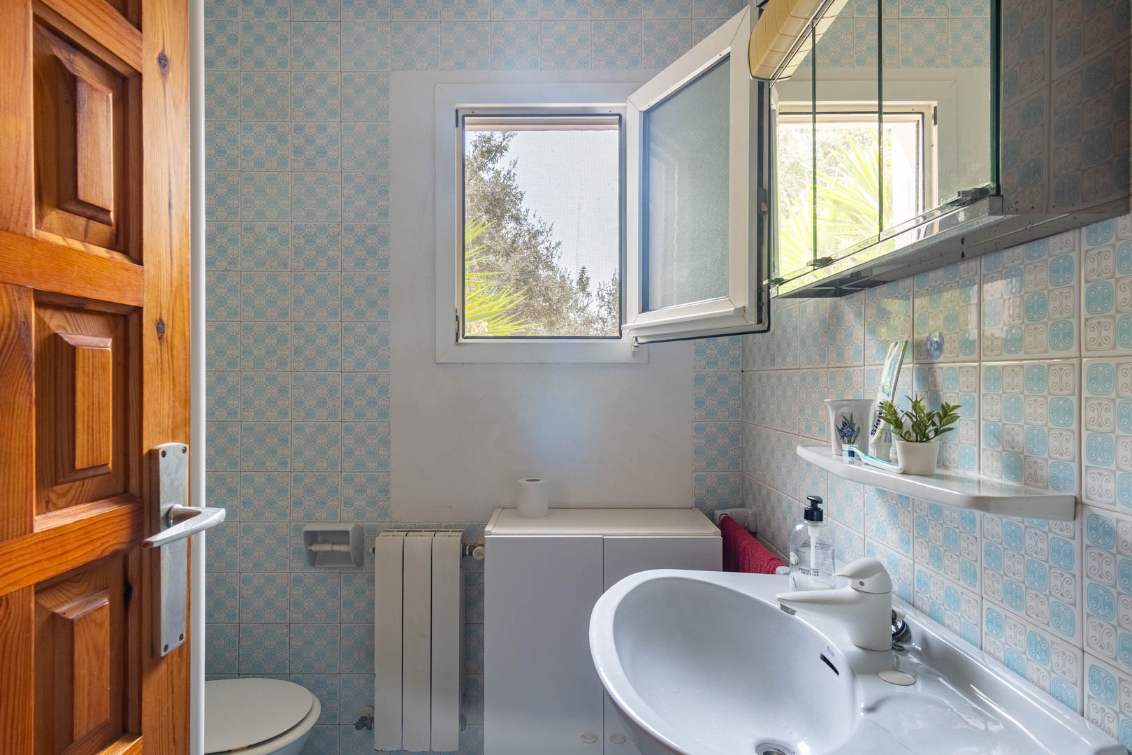 Badkamer met blauw gedecoreerde wandtegels, een witte wastafel en een draaikiepraam met hor voor natuurlijke lichtinval en ventilatie.
