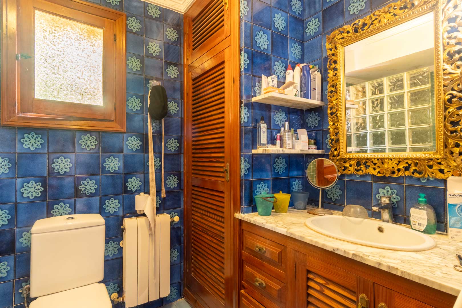 Badkamer met blauwe patroontegels, een houten wastafelmeubel met marmeren blad en een klassieke goudkleurige spiegel met bewerkte lijst.