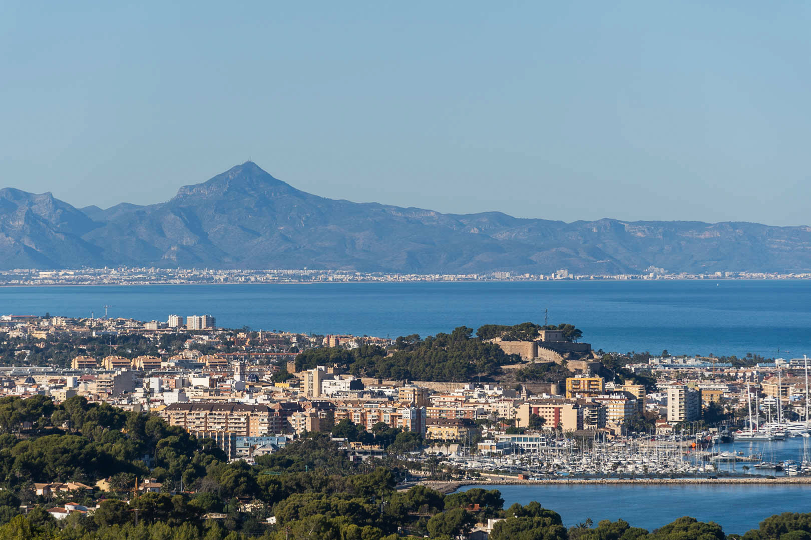 Panoramisch uitzicht op Dénia met het historische kasteel, de jachthaven en de Middellandse Zeekust tegen de achtergrond van de bergen.