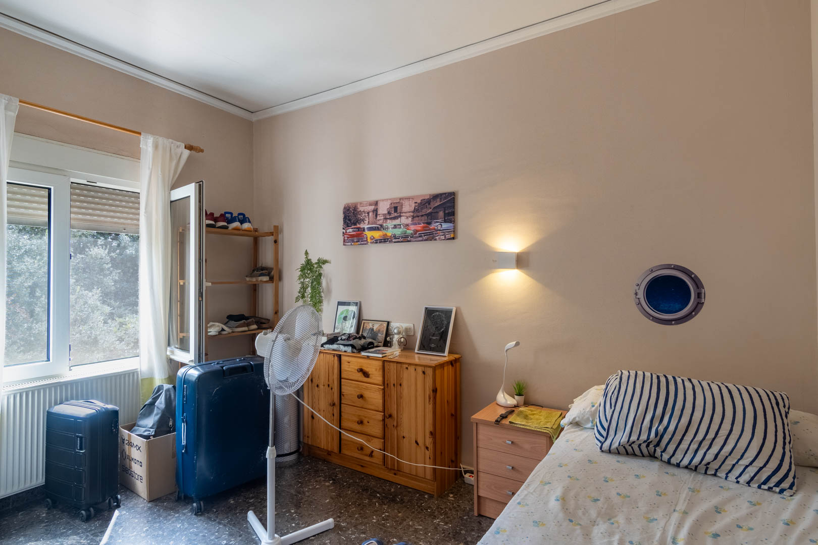 Slaapkamer met terrazzovloer, natuurlijk houten meubilair en een raam voor daglicht. Voorzien van een radiator en wandverlichting.