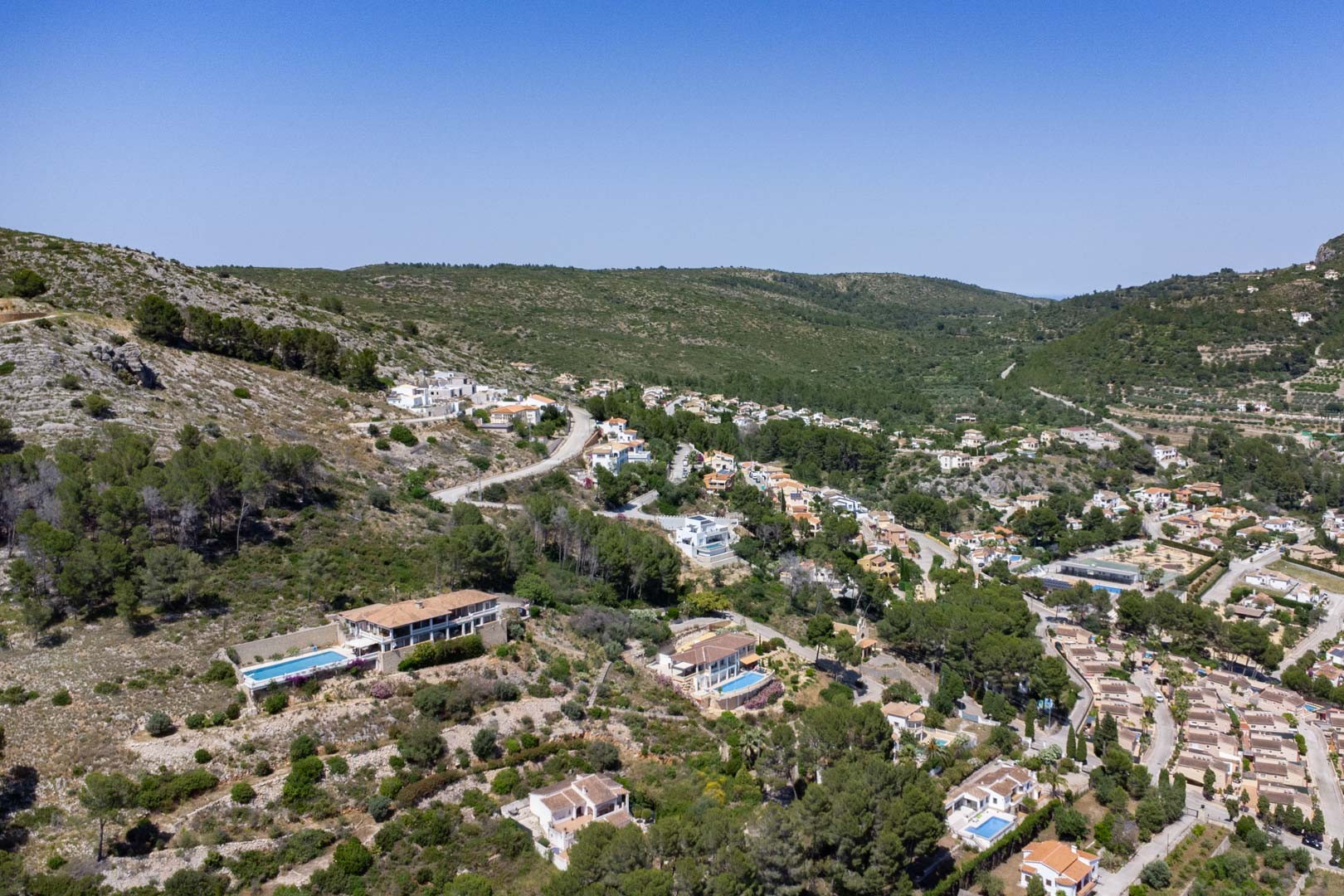 Luchtfoto van de verhoogde woonwijk in Alcalalí, die de integratie van de villa's op de helling van de Jalón-vallei toont te midden van mediterrane begroeiing.