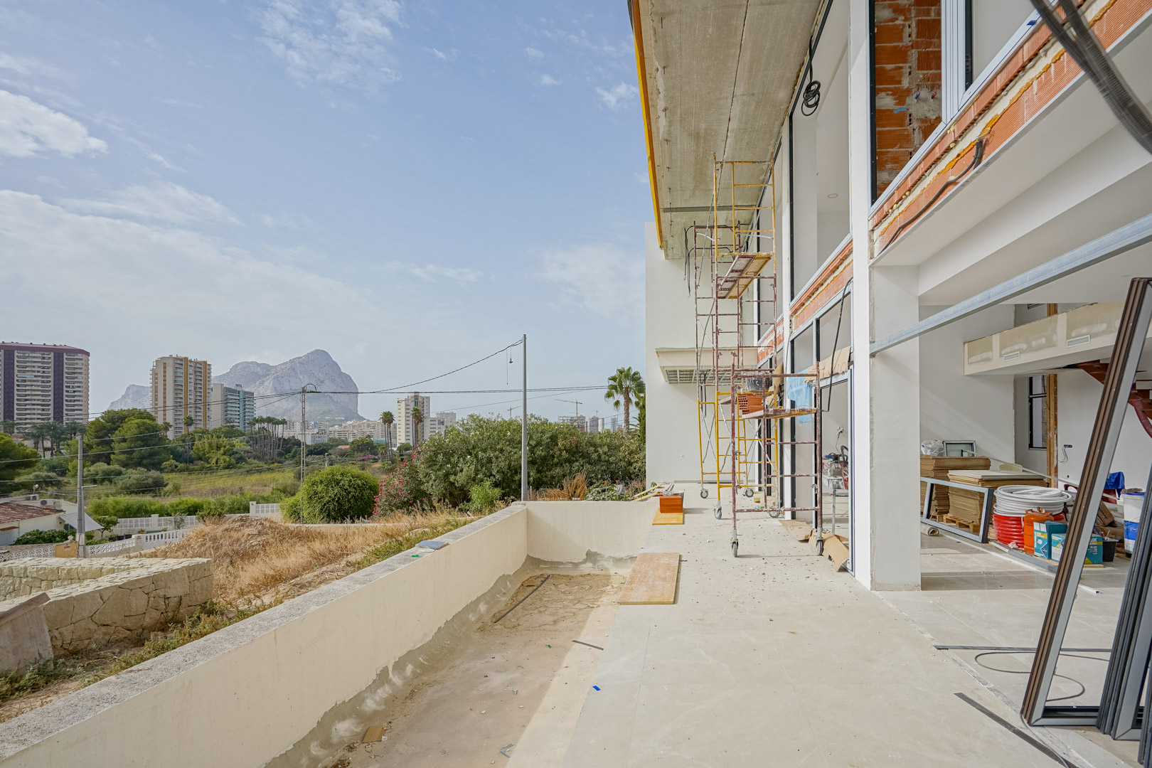 Buitenaanzicht van de villa in aanbouw met steigers, grote raampartijen en een terras met uitzicht op de Peñón de Ifach in Calpe.