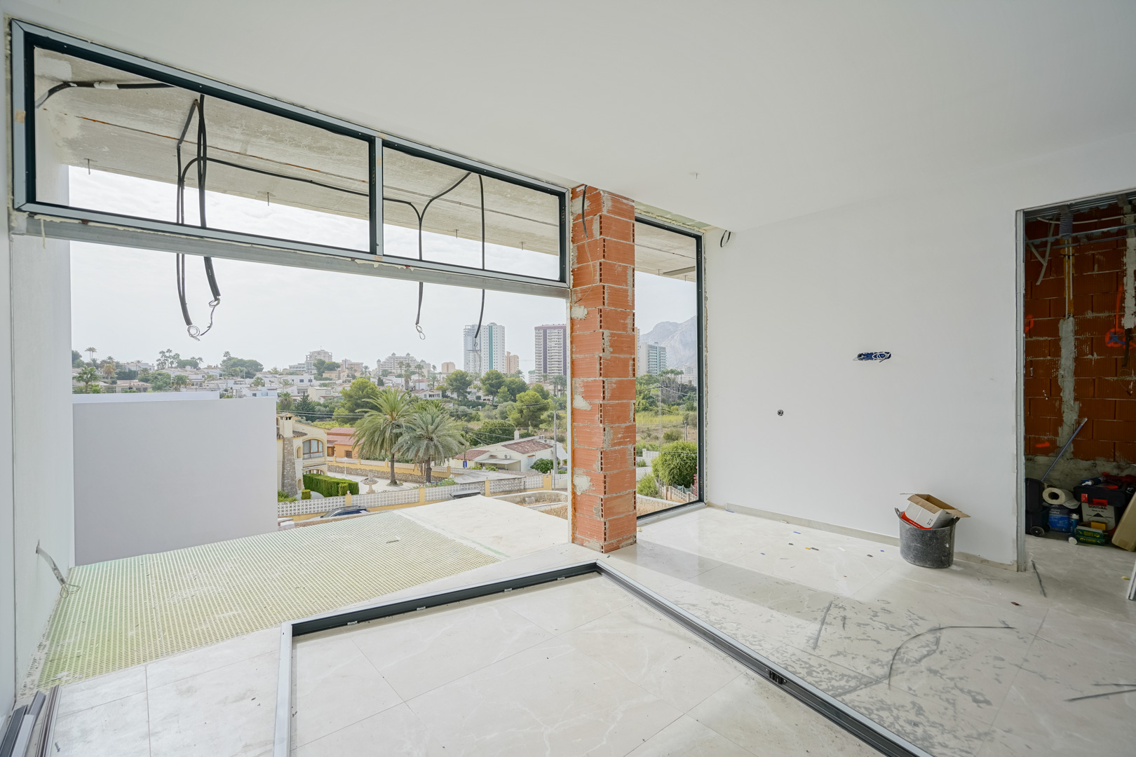 Interieur in opbouw met grote raamkozijnen die een panoramisch uitzicht bieden op de Peñón de Ifach en de skyline van Calpe.