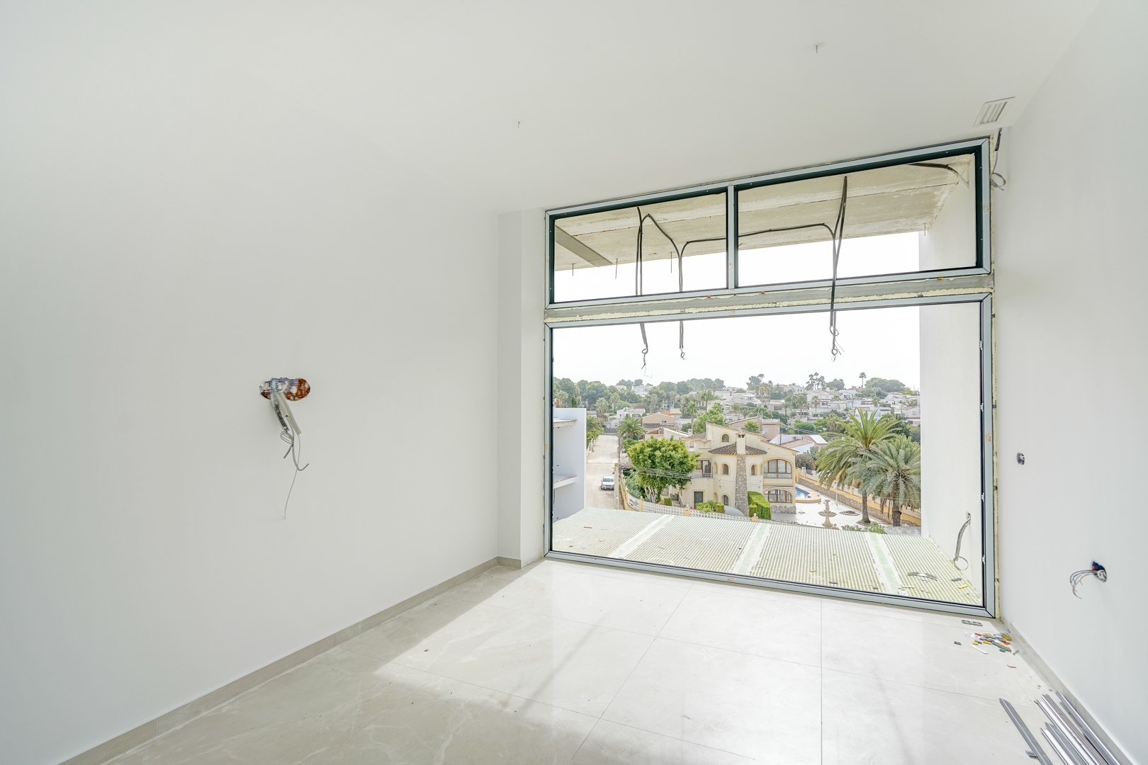 Kamer in aanbouw met kamerhoge ramen, lichte porseleinen tegelvloer en vrij uitzicht over de woonwijk Partida La Merced in Calpe.