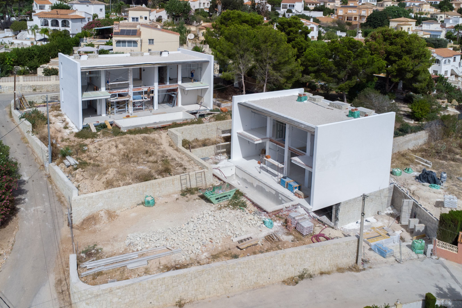 Luchtfoto van de bouwfase van de moderne villa's, met de witte betonstructuren, stenen omheiningsmuren en de percelen in volle ontwikkeling.