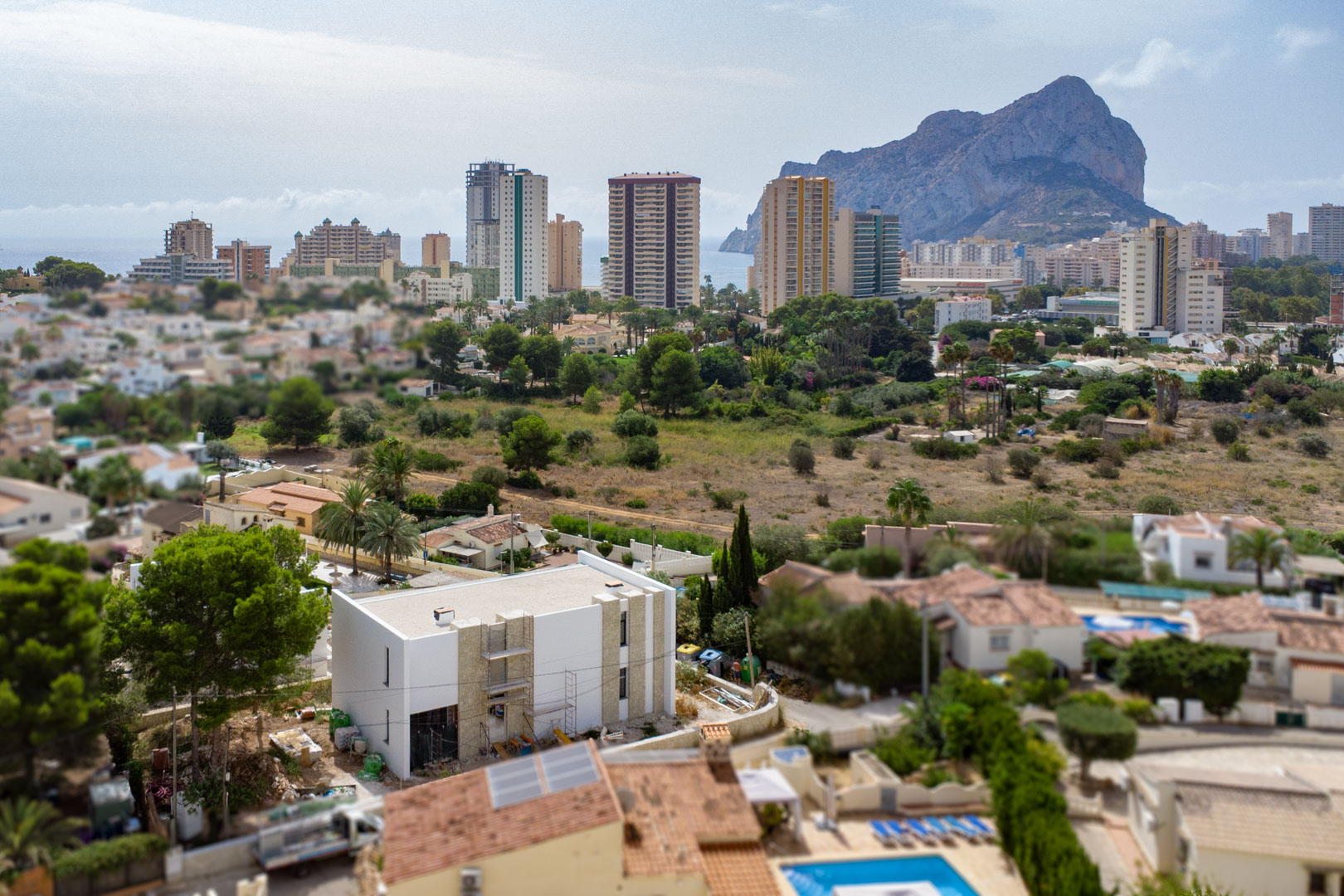 Luchtfoto van de villa in aanbouw met witte gevels en natuursteen, met een weids uitzicht op de Peñón de Ifach en de skyline van Calpe.
