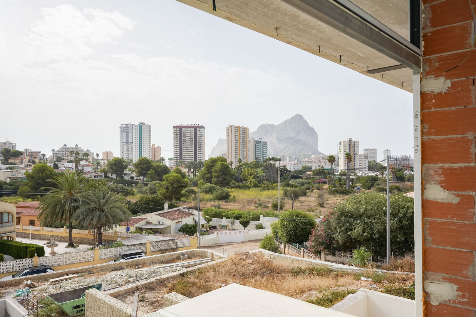 Panoramisch uitzicht vanaf de bovenverdieping in aanbouw op de Peñón de Ifach en de skyline van Calpe, omlijst door bakstenen muren en betonvloeren.