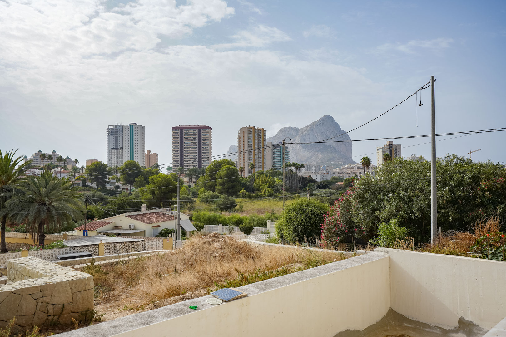 Vrij uitzicht op de Peñón de Ifach en de skyline van Calpe vanaf het verhoogde perceel van de toekomstige villa, omgeven door groen.