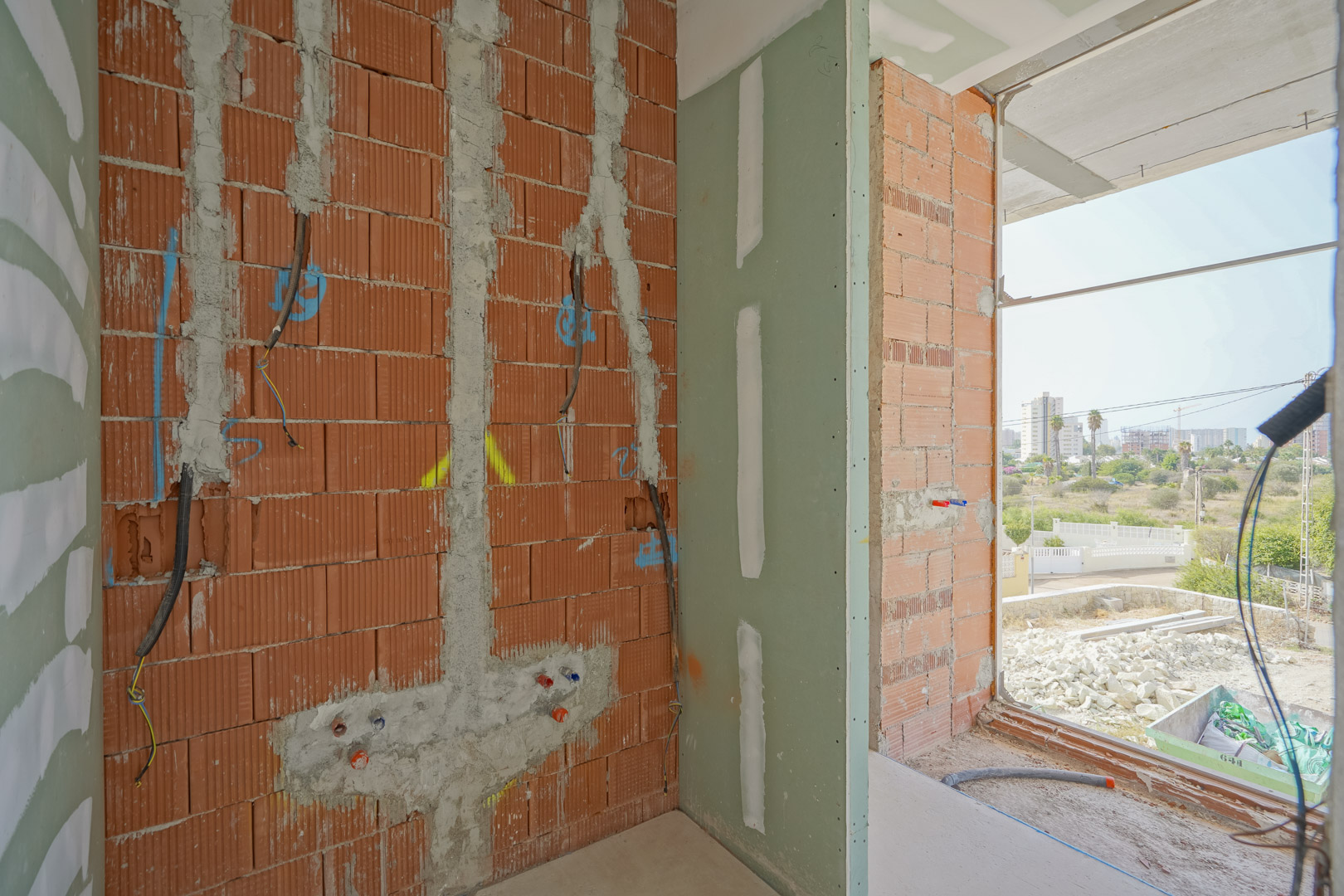 Binnenaanzicht van de ruwbouw met bakstenen muren, elektriciteitskabels en sanitaire voorzieningen naast een grote raamopening.