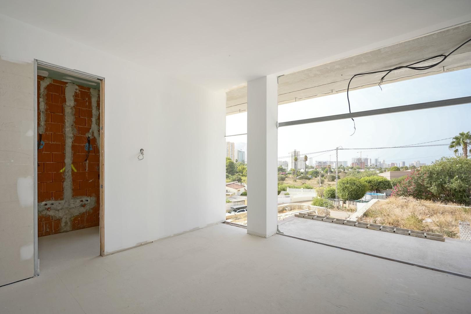 Binnenaanzicht van een kamer in ruwbouw met grote raamopeningen die uitkijken over de skyline van Calpe en de Peñón de Ifach.